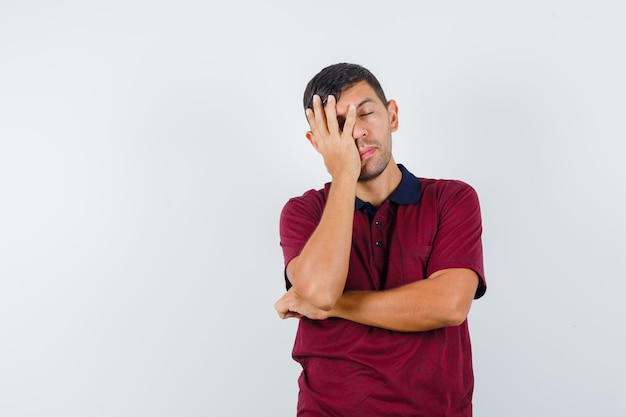 Jeune homme en t-shirt tenant la main sur le visage et l'air endormi, vue de face.