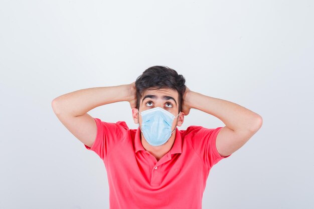 Jeune homme en t-shirt tenant les mains derrière la tête et l'air anxieux, vue de face.