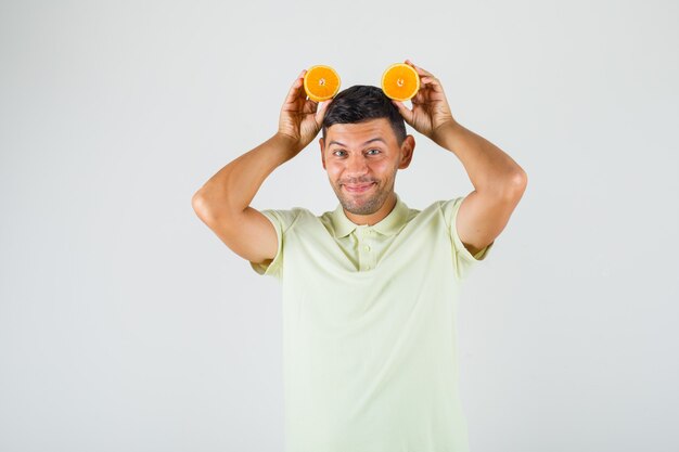 Jeune homme en t-shirt tenant des tranches d'orange sur sa tête et à la drôle