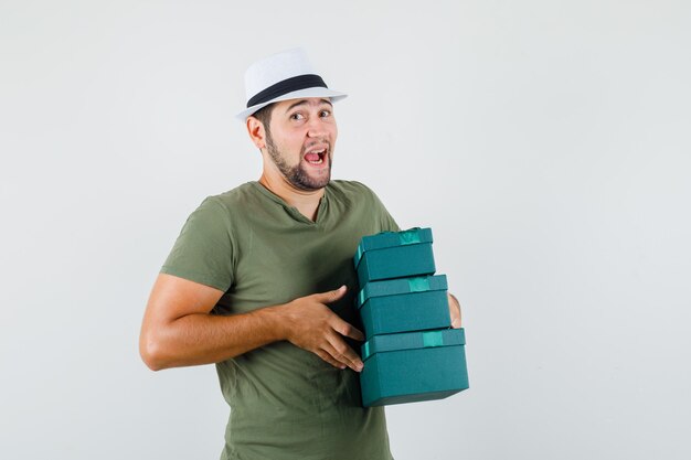 Jeune homme en t-shirt vert et chapeau tenant des boîtes présentes et à la bonne humeur