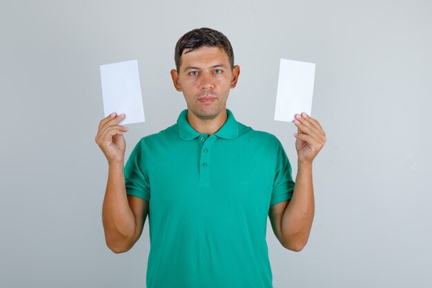 Jeune homme en t-shirt vert tenant des feuilles de papier vierges, vue de face.