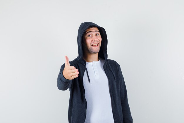 Jeune homme en t-shirt, veste donnant la main pour secouer et regarder joyeux, vue de face.