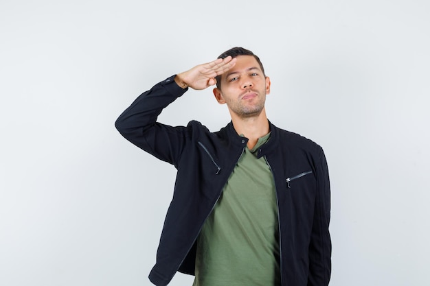 Jeune homme en t-shirt, veste faisant un geste de salut et l'air confiant, vue de face.