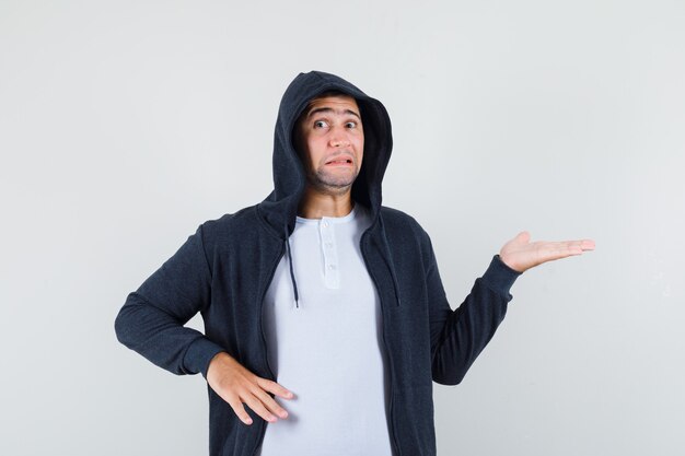 Jeune homme en t-shirt, veste faisant semblant de montrer quelque chose et l'air effrayé, vue de face.