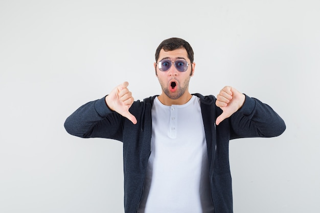 Jeune homme en t-shirt, veste montrant le double pouce vers le bas et à la vue de face.