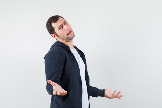 Jeune homme en t-shirt, veste montrant un geste impuissant et à la confusion, vue de face.