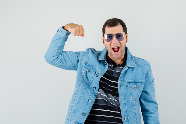 Jeune homme en t-shirt, veste montrant les muscles du bras et à la recherche d'énergie