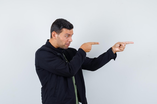 Jeune homme en t-shirt, veste pointant sur le côté et l'air concentré, vue de face.