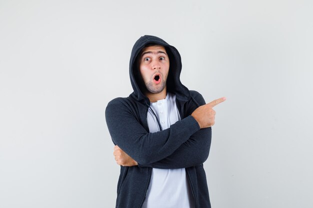 Jeune homme en t-shirt, veste pointant vers le côté droit et à la surprise, vue de face.