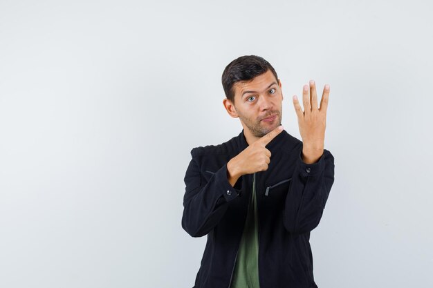 Jeune homme en t-shirt, veste pointant vers le numéro quatre par ses doigts, vue de face.