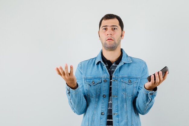 Jeune homme en t-shirt, veste tenant la calculatrice et à la confusion