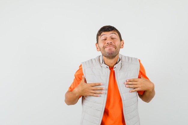 Jeune homme en t-shirt, veste tenant les mains sur la poitrine et à la vue de face, paisible.