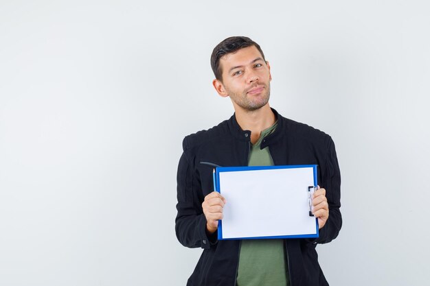 Jeune homme en t-shirt, veste tenant le presse-papiers et l'air optimiste, vue de face.