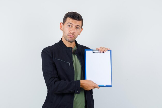 Jeune homme en t-shirt, veste tenant le presse-papiers et semblant sensible, vue de face.