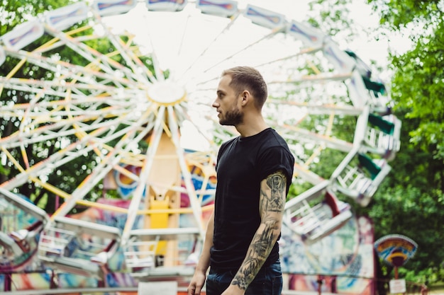 Photo gratuite jeune homme tatoué dans un parc d'attractions sur le fond d'un manège