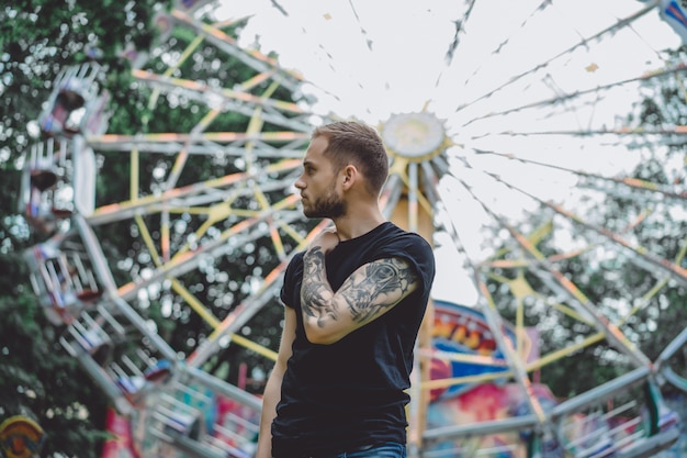 Jeune Homme Tatoué Dans Un Parc D'attractions Sur Le Fond D'un Manège