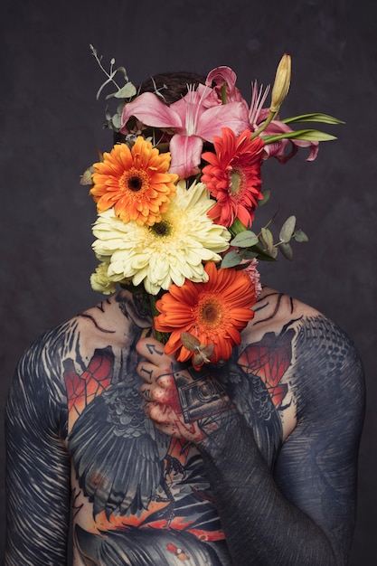 Jeune homme tatoué, nez et oreilles percés, tenant un bouquet de fleurs devant son visage