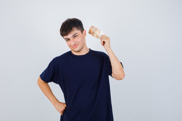 Jeune homme tenant un billet d'euro en t-shirt noir et à la confiance. vue de face.