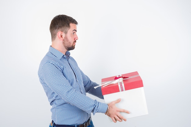 Jeune homme tenant une boîte-cadeau en chemise et à la perplexité. vue de face.