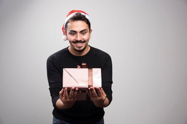 Un jeune homme tenant une boîte-cadeau sur un mur gris.