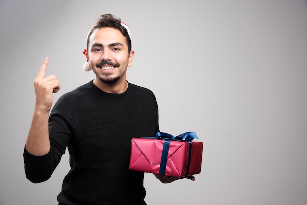 Un jeune homme tenant une boîte-cadeau sur un mur gris.