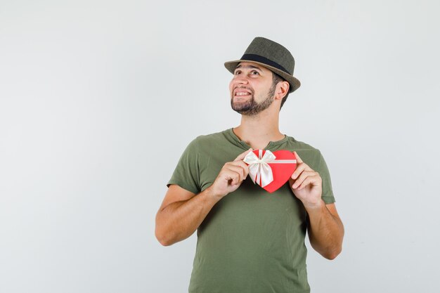 Jeune homme tenant une boîte-cadeau tout en regardant en t-shirt vert et chapeau et à la joyeuse