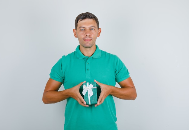 Jeune homme tenant la boîte présente et souriant en t-shirt vert, vue de face.