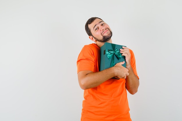 Jeune homme tenant une boîte présente en t-shirt orange et ayant l'air mignon. vue de face.