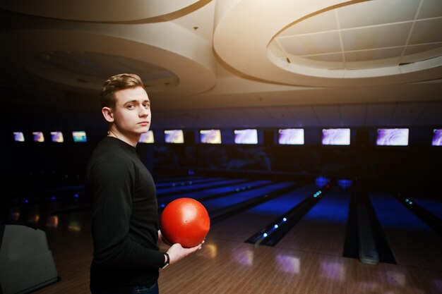 Jeune homme tenant une boule de bowling debout contre les pistes de bowling avec lumière ultraviolette