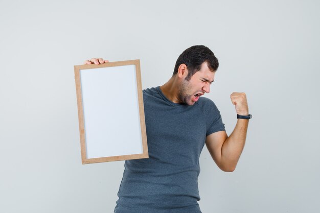 Jeune homme tenant un cadre vide en t-shirt gris et à la béatitude