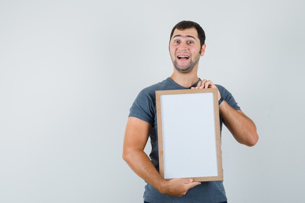 Jeune homme tenant un cadre vide en t-shirt gris et à la recherche de plaisir