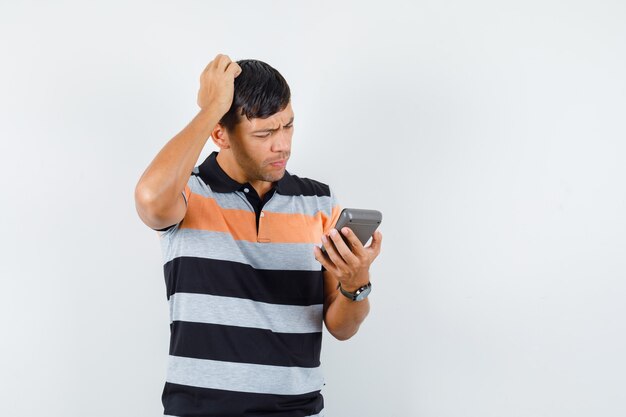 Jeune homme tenant la calculatrice tout en se grattant la tête en t-shirt et à la pensif