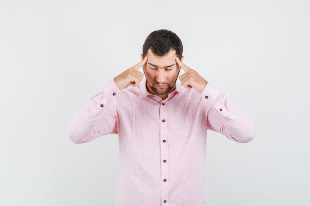 Jeune homme tenant les doigts sur les tempes en chemise rose et à la réflexion