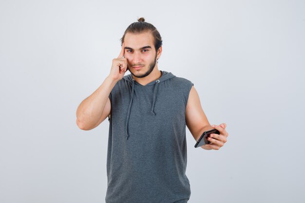 Jeune homme tenant les doigts sur les tempes en t-shirt à capuche et à la vue réfléchie, de face.