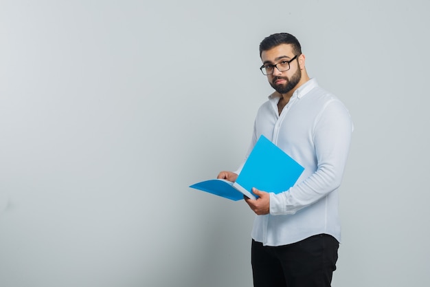 Jeune homme tenant un dossier ouvert en chemise blanche, pantalon et beau