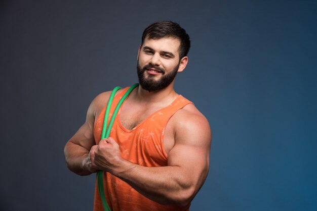 Jeune homme tenant du caoutchouc pour le sport sur un mur bleu foncé.