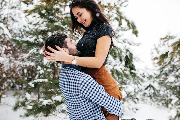 Photo gratuite jeune homme tenant une femme dans les bras dans la forêt d'hiver