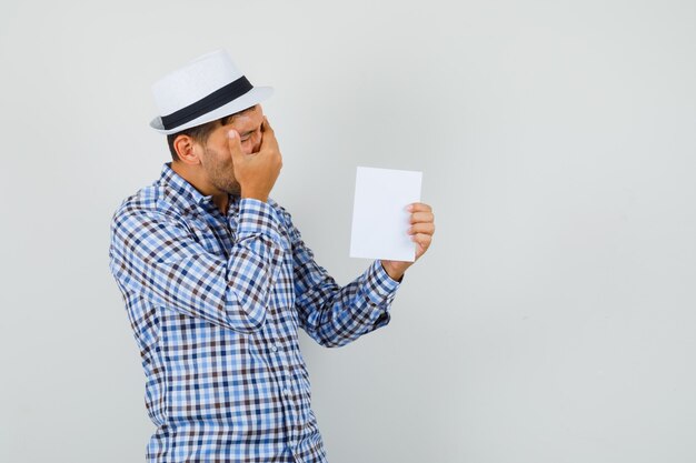 Jeune homme tenant une feuille de papier en chemise à carreaux