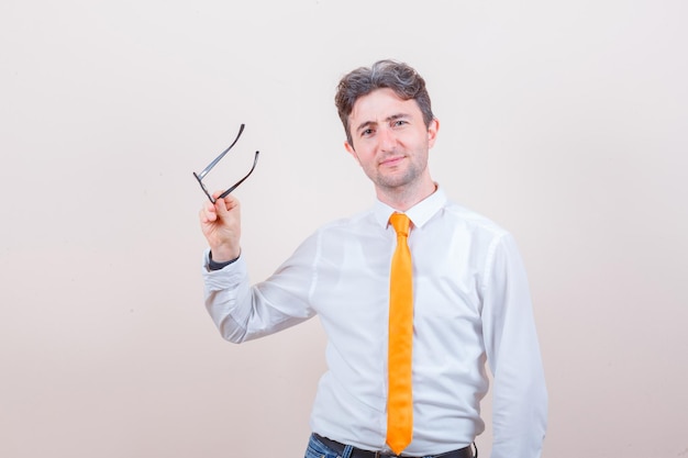 Jeune homme tenant des lunettes en chemise, jeans et regardant jolly