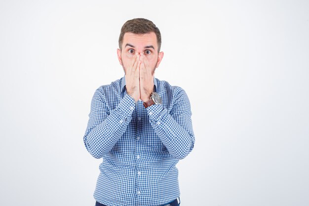 Jeune homme tenant la main sur la bouche en chemise et à la perplexité. vue de face.