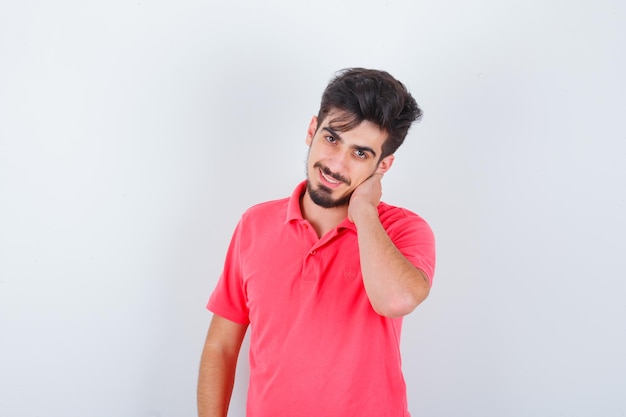 Jeune homme tenant la main sur le cou en t-shirt et l'air heureux, vue de face.