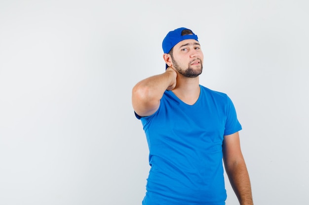 Photo gratuite jeune homme tenant la main sur le cou en t-shirt bleu et casquette et à l'élégant