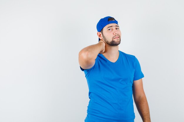 Jeune homme tenant la main sur le cou en t-shirt bleu et casquette et à l'élégant