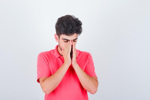 Jeune homme tenant la main dans un geste de prière en t-shirt rose et à l'air plein d'espoir, vue de face.