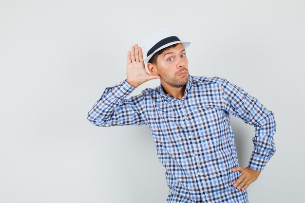 Jeune homme tenant la main derrière l'oreille en chemise à carreaux