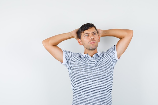 Jeune homme tenant la main derrière la tête en t-shirt et à la pensif