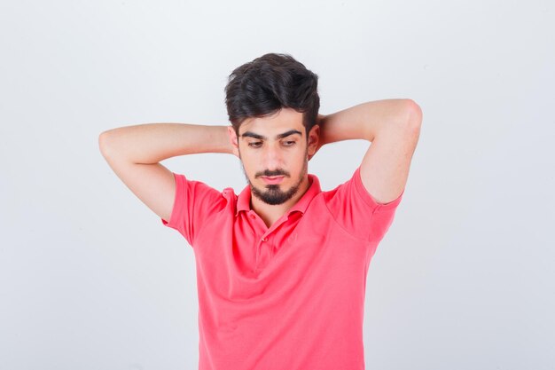 Jeune homme tenant la main derrière la tête en t-shirt rose et l'air pensif. vue de face.