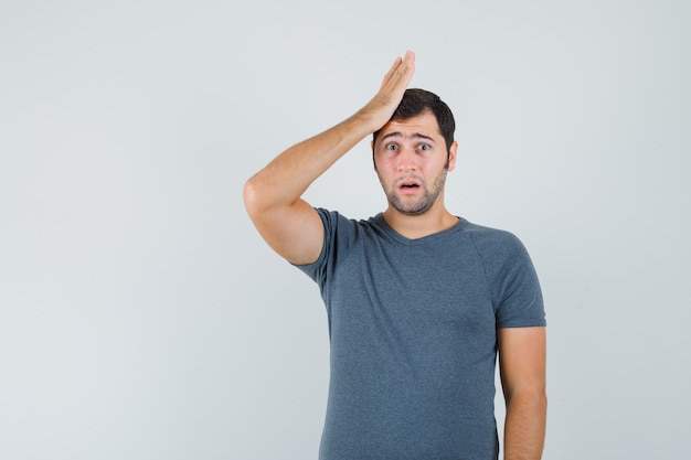 Jeune homme tenant la main levée sur la tête en t-shirt gris et à la