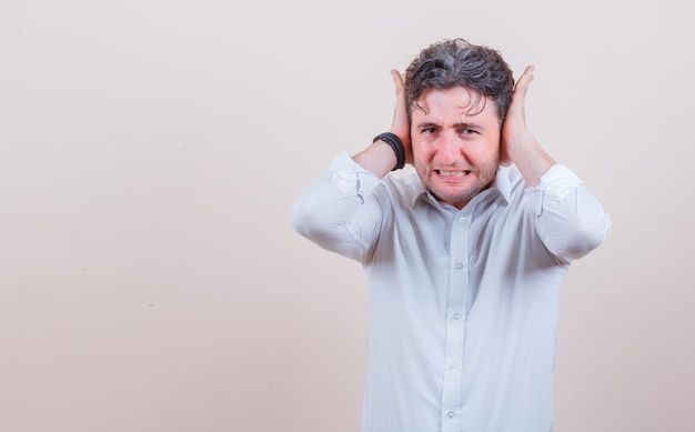 Jeune homme tenant la main sur les oreilles en chemise blanche et à l'air irrité