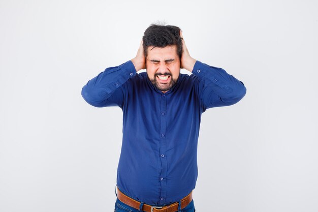 Jeune homme tenant la main sur les oreilles en chemise bleu royal et à la recherche de stress. vue de face.